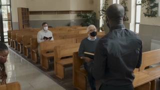 African American priest wearing protective mask greeting visitors and starting Sunday service in Catholic church