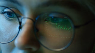 Panning right extreme close up of female investor studying cryptocurrency graphs indoor at night