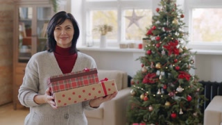 Portrait of joyful woman with presents, smiling by Christmas tree