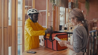 Medium wide shot of two workers. Delivery man receives his order from restaurant staff member and leaves