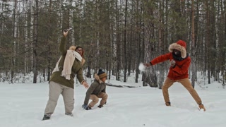 Slow motion long shot of cheerful Black woman taking photos of her family playing snowballs on snowy winter day