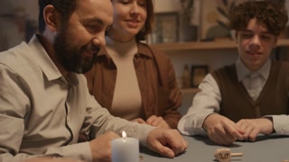 Medium close-up shot of Jewish man in yarmulke playing dreidel with his teenage son and adult daughter at Hanukkah, spinning it and getting Hebrew letter Gimel, meaning whole