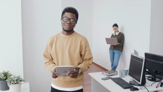 Focused shot of young man in stylish attire holding tablet in modern office