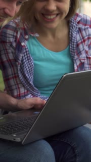 Students collaborate on a laptop while seated on a bench