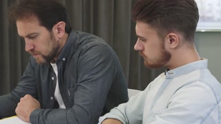 Colleague Conversation: Bearded Young Man and Mature Colleague at the Office