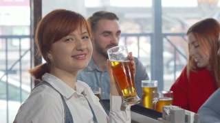 Charming woman smiling to the camera while drinking delicious beer