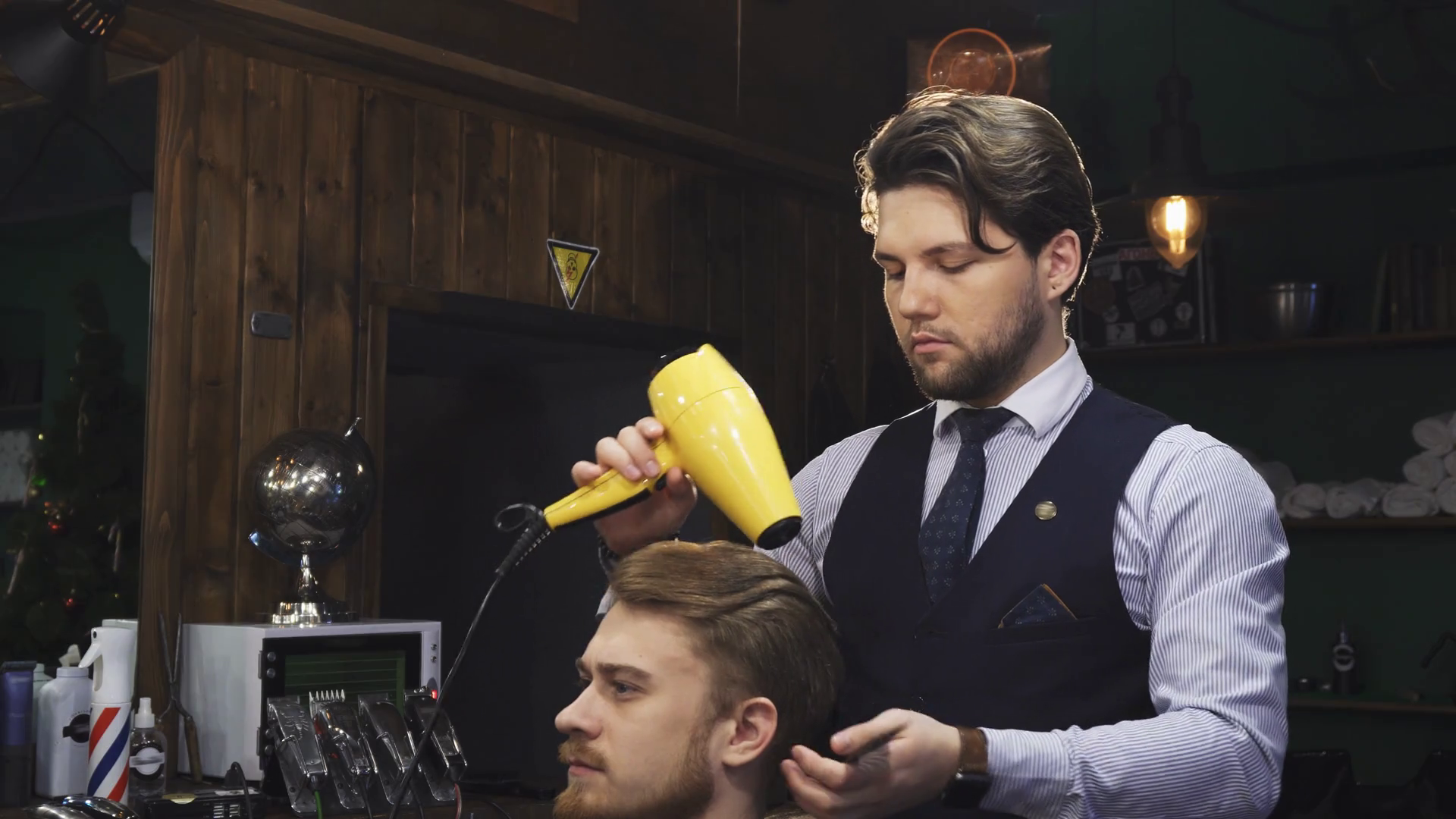 Young handsome professional barber drying and styling hair of his