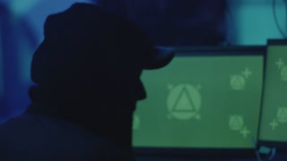 Man in the cap is sitting and working on stealing data at the computer as haker. Hideout Place has Dark Atmosphere.