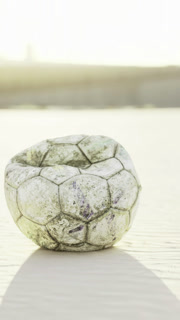 Worn soccer ball resting on sandy ground in bright sunlight during day