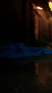 Blue fabric lies on wet ground near a building at night