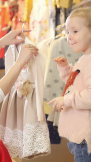 Shopping for kids - cute little girl with mommy buying dress in store of kids clothes