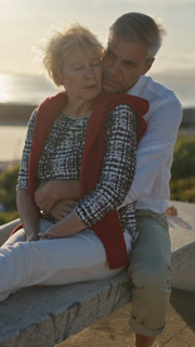 Senior couple embracing on bench at sunset by the sea