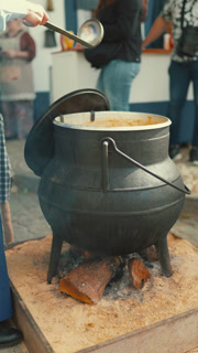 People gather around a large pot cooking food at a market in the afternoon sun