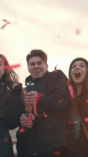 Group of friends having fun with party poppers confetti outdoors - slow-motion