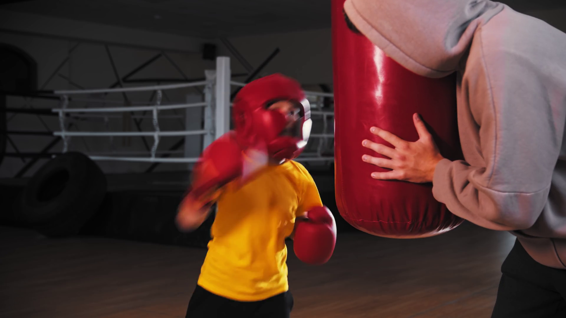 Little boy in protective helmet hitting the punching bag while the