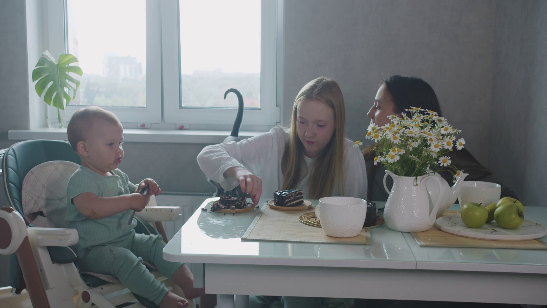 A cute family of mother and two daughters eating cake and feeding a