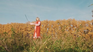 Woman in red national dress training fencing with a sword on the field