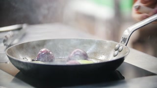 Cook sautés onions in a frying pan, showcasing chef's hand