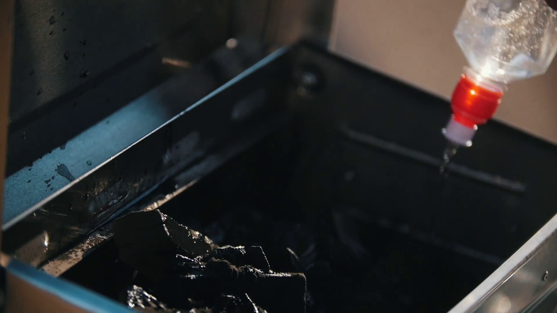 Portative grill. A man pouring out the charcoal lighter fluid on the