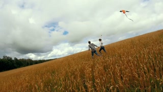 Stedicam slow-motion - loving teenagers running with kite on the wheat field at summer cloudy day