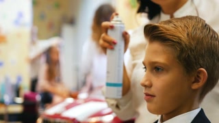 Stylist styles young boy's hair with spray