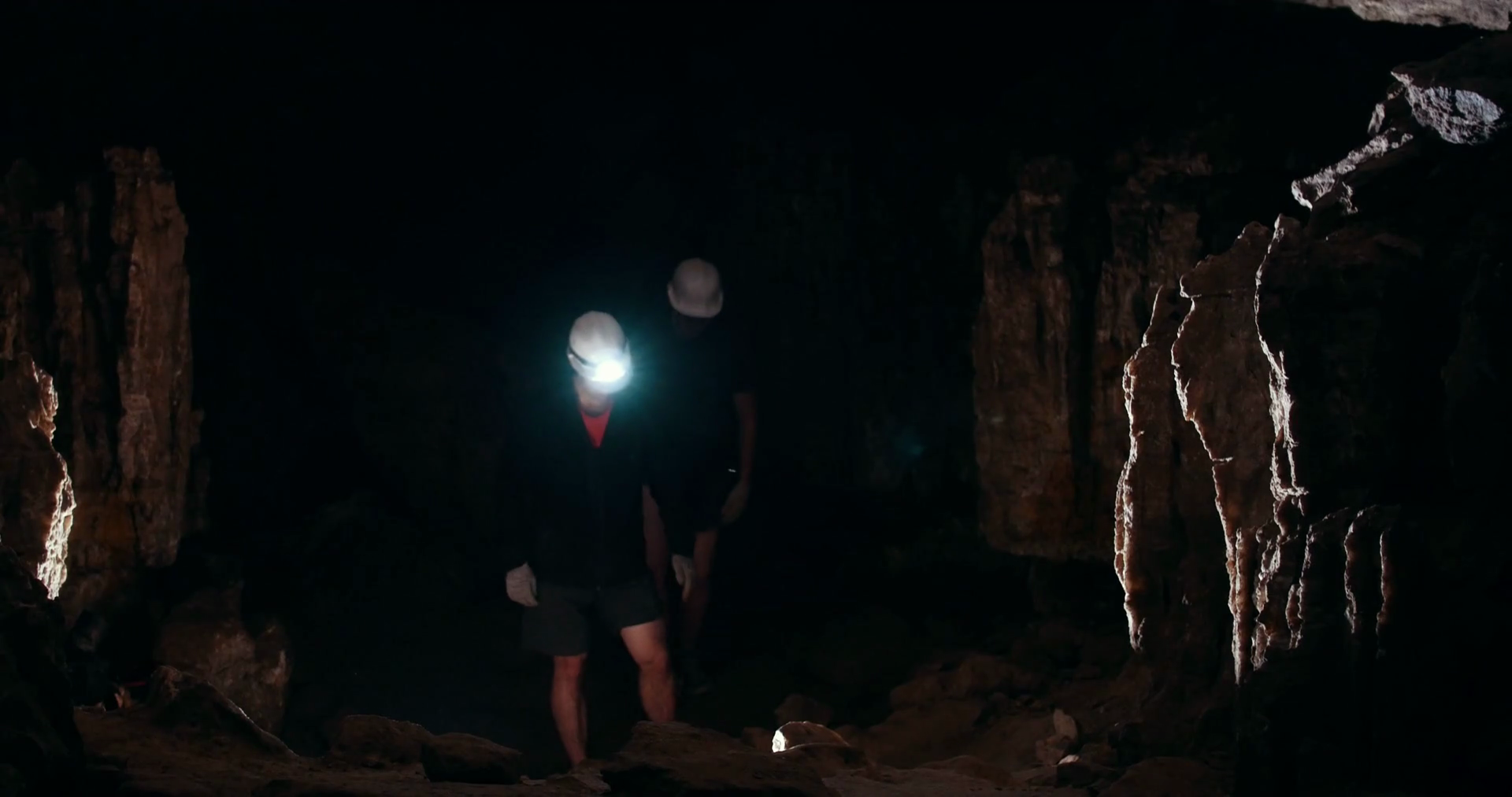 Two young men speleologists with flashlight walks in a dark cave Stock