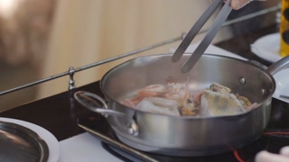The chef on the terrace of the summer restaurant stirs the frying sea creatures in a frying pan.