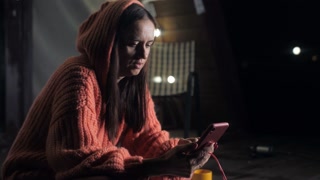 A woman on the porch of the house in the evening uses a smartphone