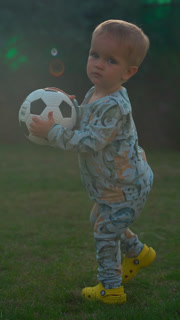 Vertical Of Cute Blond Boy Holds Soccer Ball Walking On Green Grass - Professional Stock Footage