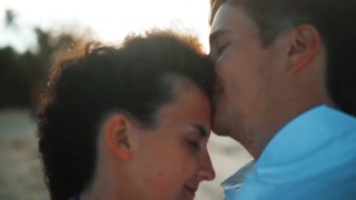 Happy couple kissing at sunset on tropical island in honeymoon holiday. Blurred beach and ocean.
