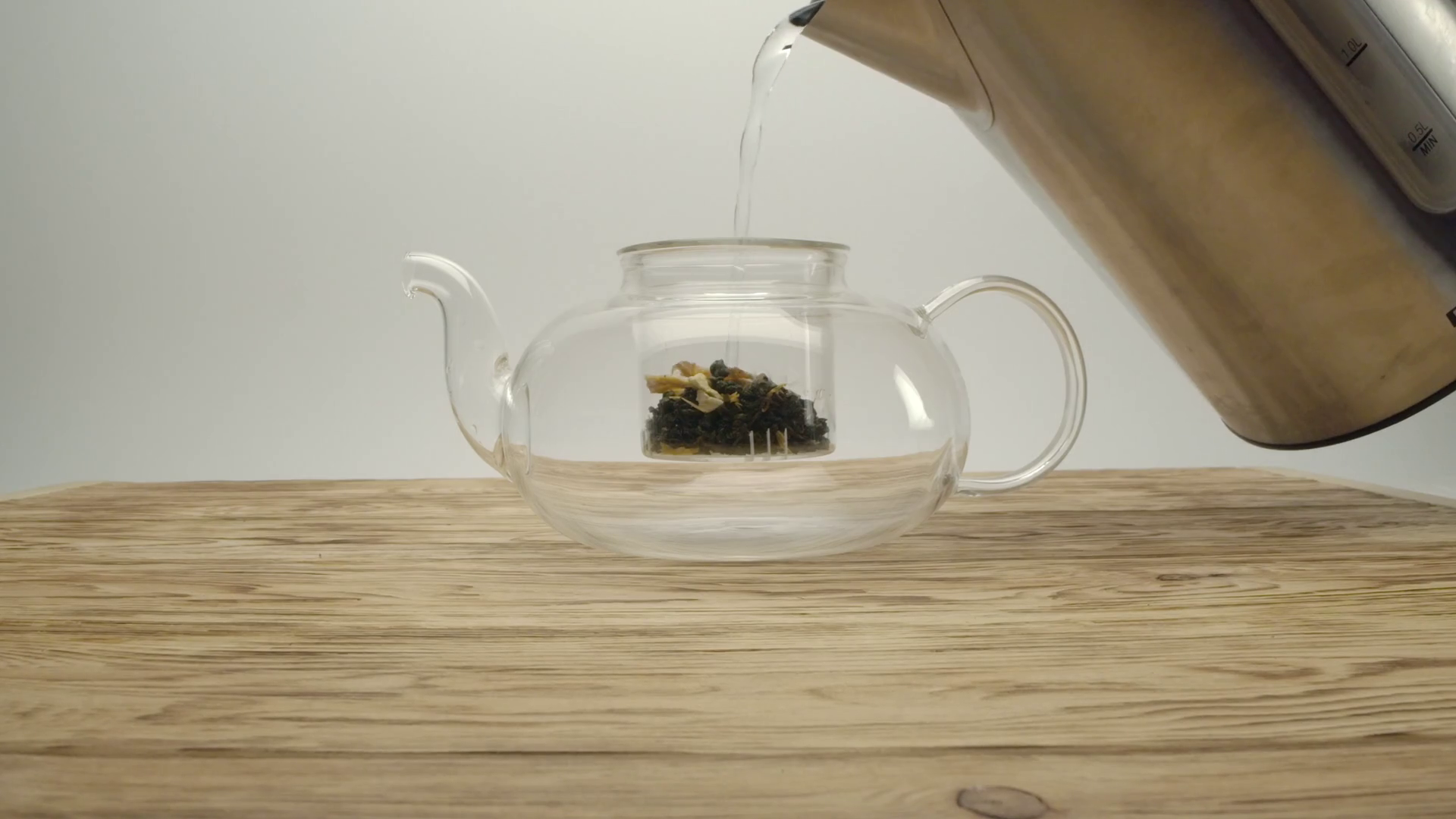 Pouring boiling water from kettle into white tea in a teapot on a
