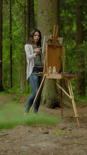 Vertical of General wide shot of a cute artist painting a landscape on an easel in the forest. - Professional Stock Footage