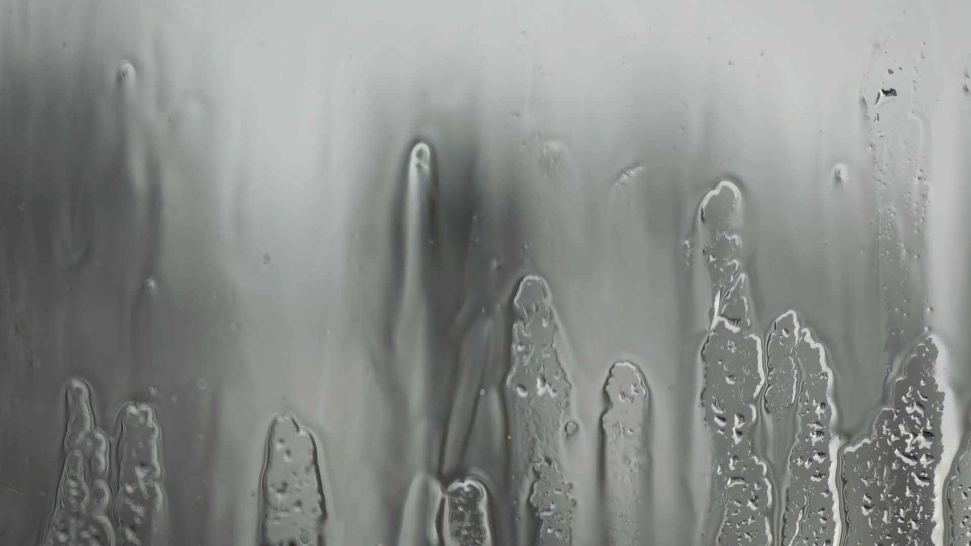 Close up view of rain drops trickling down on glass surface with blue