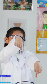 Young Asian Girl in Lab Coat Pointing Down in Science Classroom