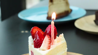 Strawberry Shortcake Slice with Lit Birthday Candle on Wooden Plate