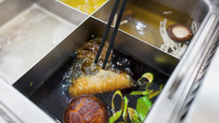 Chopsticks Lifting Fried Tofu Skin from Boiling Asian Hot Pot Soup