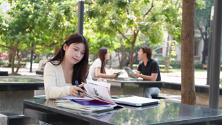 Young Thai University Student Studying with Textbook and Laptop on Campus