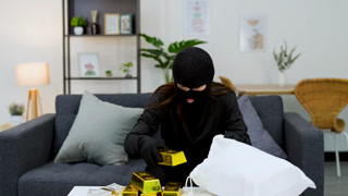 Masked Burglar Stealing Gold Bars and Cash in a Living Room