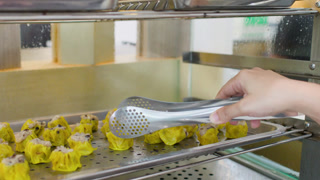 Person Using Metal Tongs to Pick Up Siu Mai Dumplings