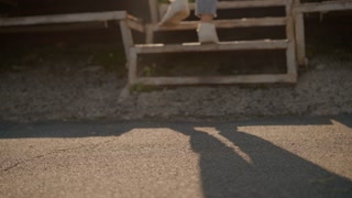 Blurred close-up leg view of person in white sneakers and jeans walking toward rusty staircase and climbs it with individual shadow cast on