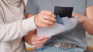 Garment makers standing close together carefully checking different material types from sample sheets during creative collaboration