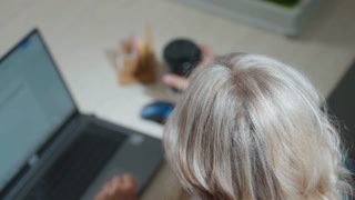 Top down view of woman working on laptop pauses typing to sip from black cup then resumes, seated at desk with visible screen, organized