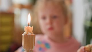Close up of candle with melted wax glowing warmly in front of blurred view of toddler making funny gesture while eating, suggesting playful