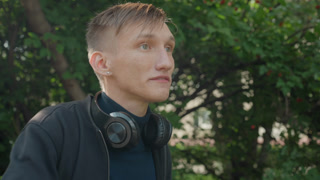 young man with headphones in rain, wet hair and raindrops on skin, candid outdoor portrait in leafy park, subtle cinematic lighting