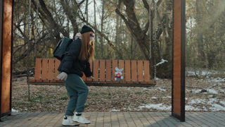 Sneaking along snowy park bench, backpacked person furtively approaches and snatches small object, cautious glances, cold late afternoon