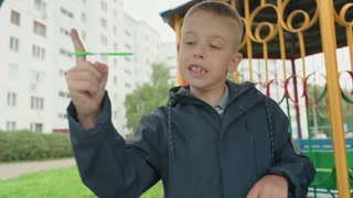 Child displays scissors. Boy with scissors at playground. Child holds scissors up happily at park gazebo. Young boy demonstrates scissors to