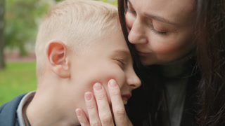 Boy and mother preparing for school outdoors, playful morning hug and closeup smiles, supportive parent comforting child on park bench