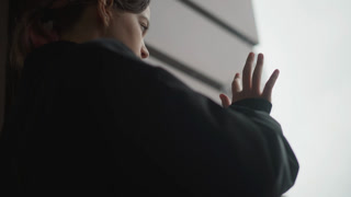 Girl says goodbye. Young woman with backpack gazes outside. Silhouette of girl watching rain from window with backpack. Girl waving farewell