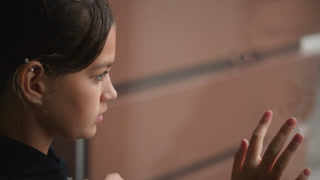 Young girl gazes at raindrops on glass pane. An adolescent girl softly focuses on rain slipping down window. Teen girl patiently observes