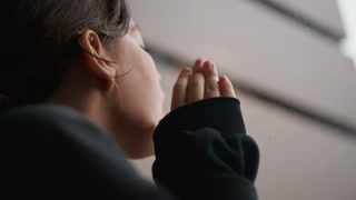 Youthful observer attentively watches rain trickle down windows in silence. Young individual patiently and quietly observes rain cascading